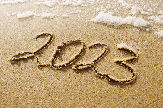 New year 2023 written on sand, beach and soft white foamy ocean wave on background. Winter holidays concept photo