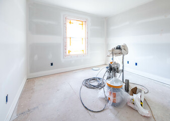 Wall painting equipment on wooden floor in empty white room with sunlight through the window at construction site. Home improvement, house renovation concept. Remodeling, paintwork service business