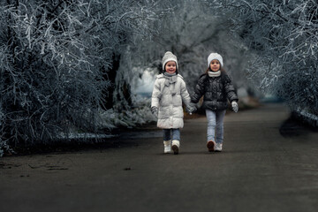 Two little girls walking through the frozen trees on cold winter day.