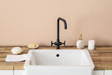 Fototapeta na wymiar Sink with bath accessories and burning candle on table near beige wall