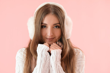 Young woman in warm ear muffs and sweater on pink background, closeup