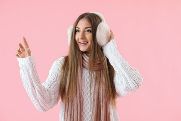 Young woman in warm ear muffs pointing at something on pink background