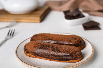 Plate with delicious chocolate eclairs on light table, closeup
