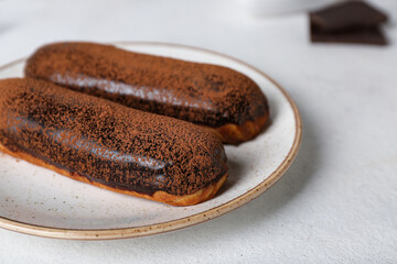 Plate with delicious chocolate eclairs on light table, closeup