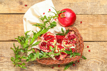 Wicker basket with fresh pomegranates and plant branches on wooden background