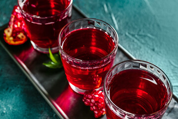 Board with glasses of fresh pomegranate juice on dark color background, closeup