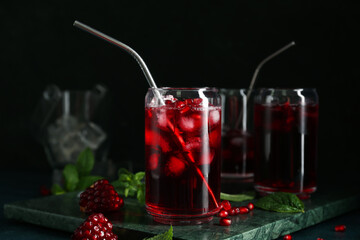 Board with glasses of cold pomegranate juice on dark background, closeup