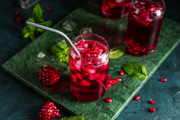Board with glasses of cold pomegranate juice on dark color background