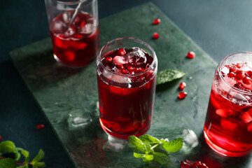 Board with glasses of cold pomegranate juice on dark color background, closeup