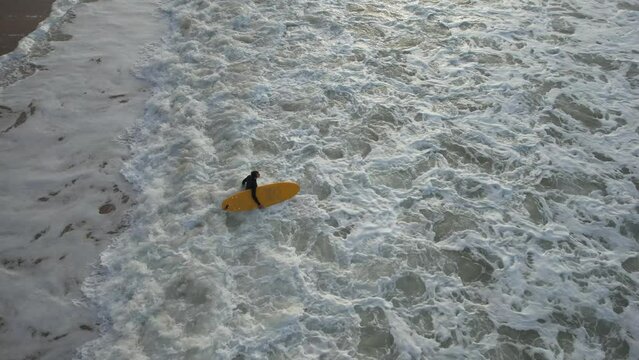 Aerial view from drone in Bidart France of a fixed shot of a surfer with a yellow surfboard that gets out of frame in the evening