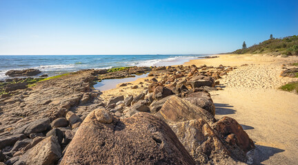 Volcanic rocky shelf with a rock pool at Point Arkwright, Coolum, Sunshine Coast, Queensland. Looking south along the sandy surf beach.