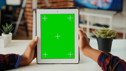 Office employee vertically holding wireless device with greenscreen display, looking at chroma key template with isolated copyspace. Using blank mock up background on digital tablet. Close up.
