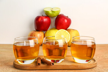 Wooden board with glasses of fresh apple juice and cinnamon sticks on color table
