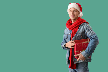 Handsome man in Santa hat with Christmas presents on green background