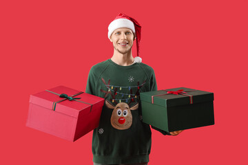 Handsome man in Santa hat with Christmas presents on red background