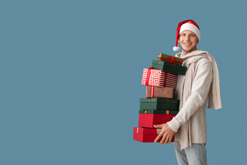 Handsome man in Santa hat with Christmas presents on blue background