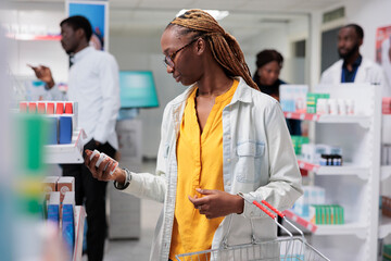 African american customer buying food supplements in drugstore, reading instruction, holding...