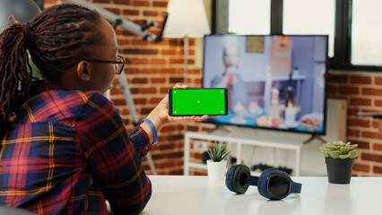 Female freelancer looking at smartphone with greenscreen, analyzing horizontal chroma key display...