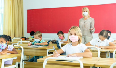 Diligent tween girl in protective mask studying in school with classmates. New life reality in coronavirus pandemic