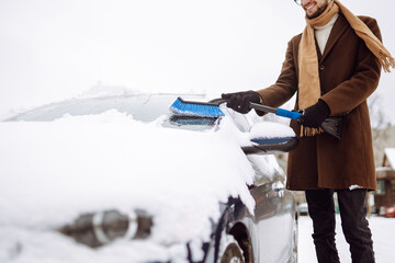 Transport, winter, weather, people and vehicle concept -  young man cleaning snow from car with...