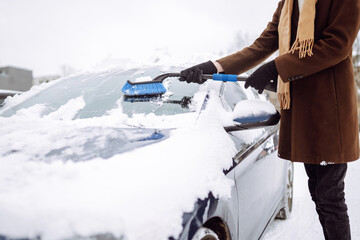 Transport, winter, weather, people and vehicle concept -  young man cleaning snow from car with brush.