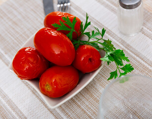Homemade savory pickled tomatoes served on plate with fresh greens. Healthy vitamin food..