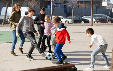 Group of children playing soccer with ball outdoors and having fun