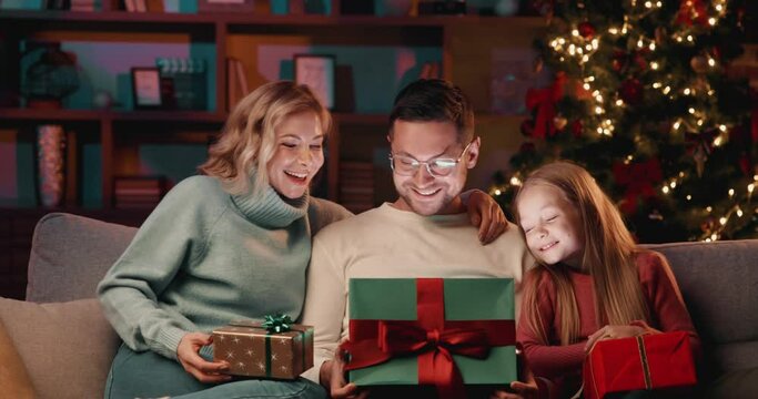 Loving parents with daughter opening gift during Christmas celebration