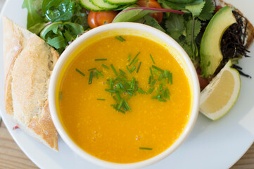 yellow pumpkin soup with fresh herbs in a bowl , plate top view