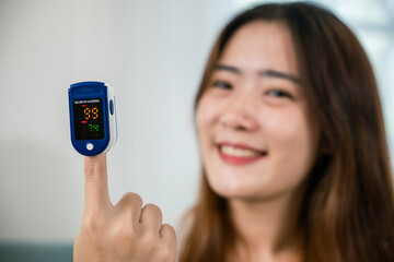 Asian young woman using medical oximeter equipment to measure pulse oxygen saturation on sofa in living room at home, Self healthcare with corona virus pandemic, medical healthcare