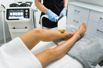closeup view woman's legs getting hair removal procedure at the beauty center, cosmetologist using...
