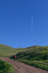 Obraz premium Female hiker walking up steep trail with con trail in the distance on a clear day at Mission Peak Park in Fremont, California