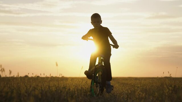 Little boy rides bicycle on grass field.Active kid, cyclist plays, rides at sunset. Childs feet are pedaling. Pedaling, bicycle wheel. Childrens travel. Physical exercise. Family in park. Free play