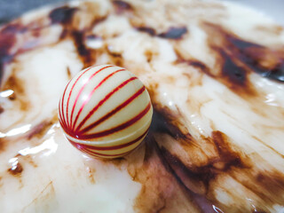 close up of a white chocolate ball with red strips, delicious white chocolate cake decorated with a chocolate ball, selective focus