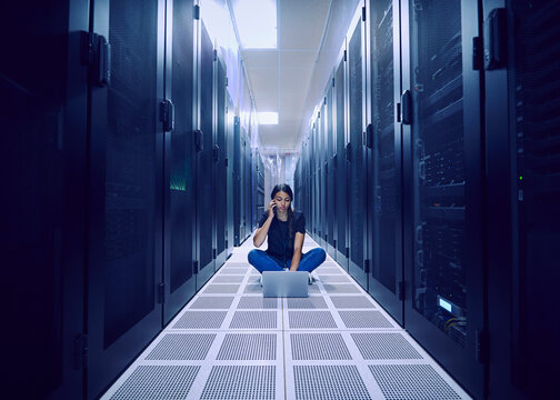 Female technician using laptop and smart phone on floor in server room