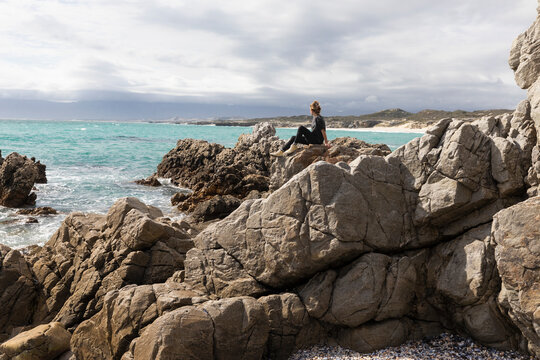 South Africa, Gansbaai, Teenage girl (16-17) sitting on rocks on sea coast