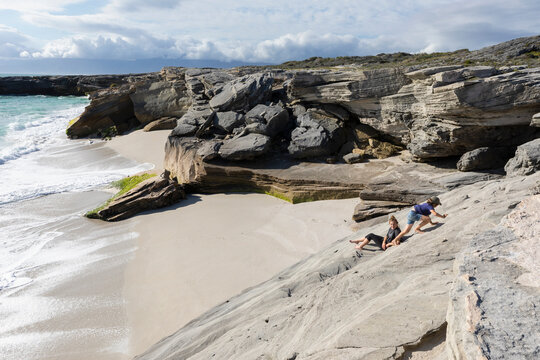 South Africa, Gansbaai, Teenage girl (16-17) with younger brother (8-9) climbing on rocks on sea coast