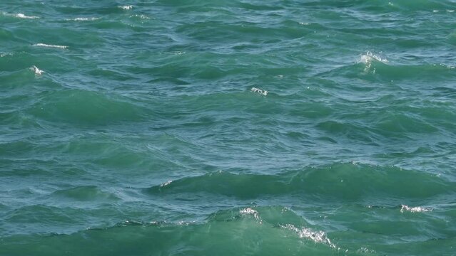 Panning up shot of rough waves on Lake Michigan with greenish blue or turquoise water as sun lights up the splashing  and sloshing water.