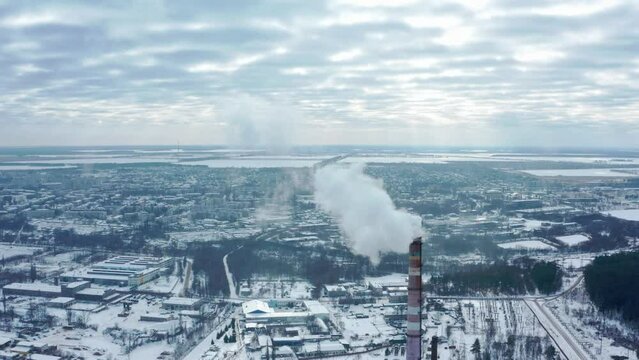 Smoking chimney on the background of the city in winter. Environmental pollution from emissions into the atmosphere. Aerial view of atmospheric emissions. Ukraine 2022, the city of Shostka.