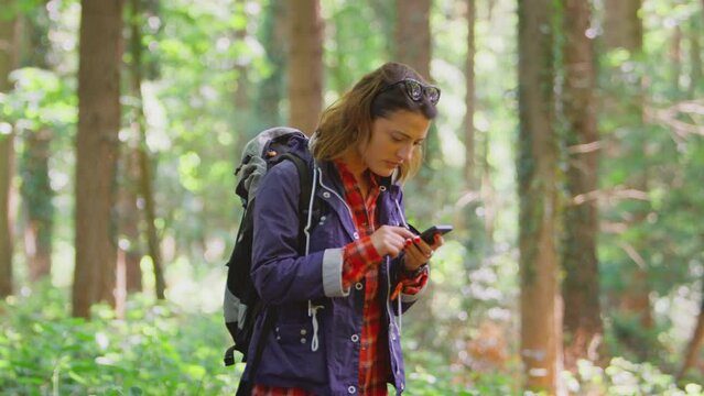Woman hiking through woods using GPS app on mobile phone to navigate - shot in slow motion