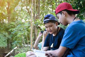 Asian boys are preparing tools and using binoculars to do the birds' watching in tropical forest during summer camp, idea for learning creatures and wildlife animals and insects outside the classroom.