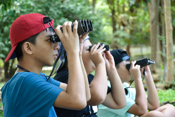 Asian boys are using binoculars to do the birds' watching in tropical forest during summer camp, idea for learning creatures and wildlife animals and insects outside the classroom.