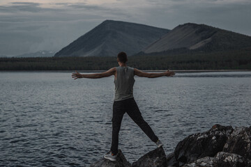 a young man with his arms outstretched stands on the shore of the lake