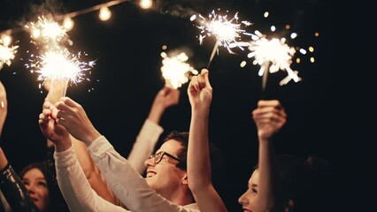 close up hands holding sparklers group of friends celebrating Christmas waving sparkler fireworks dancing enjoying new years eve party having fun holiday celebration at evening Christmas gathering. - Powered by Adobe