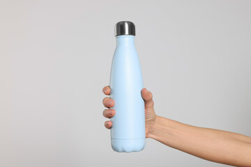 Woman holding thermo bottle of drink on light background, closeup