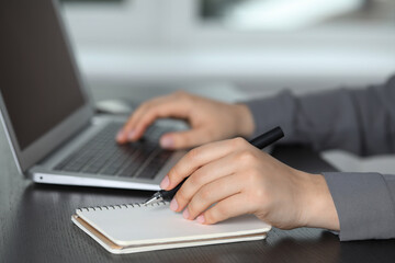Fototapeta premium Woman with pen, laptop and notebook at wooden table, closeup. Electronic document management