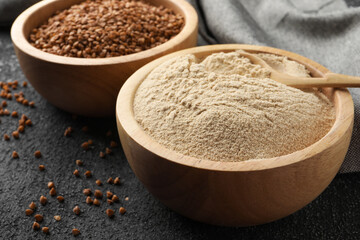 Buckwheat flour and grains in bowls on black table, closeup