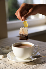 Woman taking tea bag out of cup at table indoors, closeup