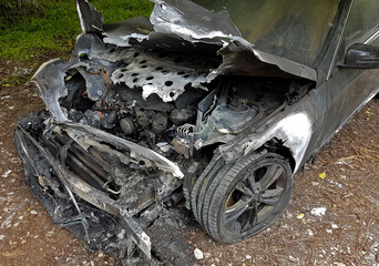 Front and side view of an abandoned burned out car with the hood left open to expose burned engine 