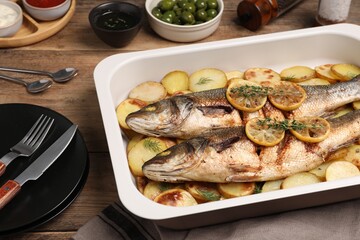 Baking tray with delicious baked sea bass fish and potatoes on wooden table